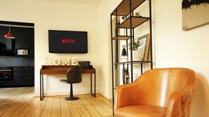 Un salon moderne avec un plancher en bois, un fauteuil en cuir, un bureau avec un ordinateur et une bibliothèque.