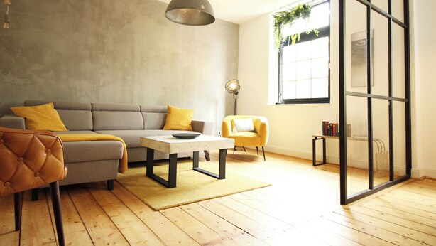 Un salon moderne avec un canapé gris, des coussins jaunes, une table basse en bois et un fauteuil jaune.