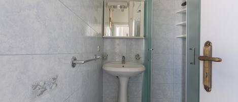 A bathroom with a pedestal sink, a mirror above it, and a door with a brass handle.