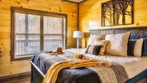 A wooden cabin bedroom with a bed, window, and artwork on the wall. - Fall Dollywood Magic! HotTub, Arcade, Game Room, Dog OK, 2 Suites, A+ location (Sevierville)
