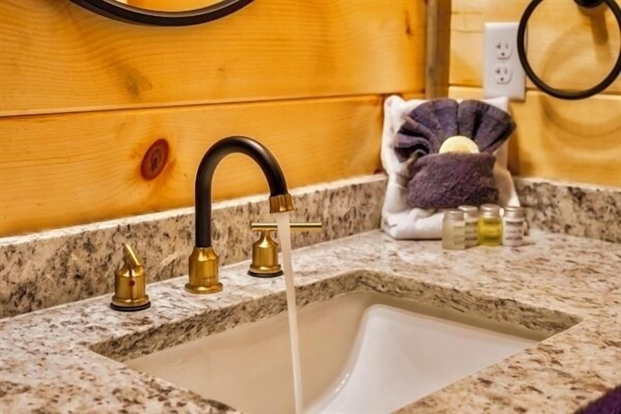 A bathroom with a granite countertop, a sink with a single faucet, and a towel rack with a towel and soap dispenser.