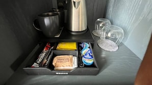 Ein ordentlich sortierter Minikühlschrank mit Kaffeemaschine, Wasserkocher, einer Serviertschale mit Snacks und einem Glasbehälter.