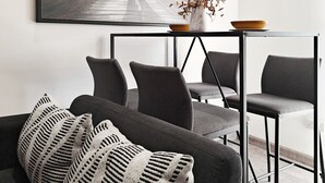 Ett modernt vardagsrum med en grå soffa, svart- och vitrandiga kuddar, ett soffbord med en vas och en skål, och en stor inramad tavla med en elefant på väggen.