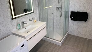 A modern bathroom with a glass-enclosed shower, a white sink with a mirror, and a black towel hanging on the wall.