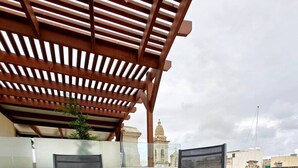 A round outdoor table with four chairs, a grill, and a pergola structure.