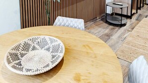 A modern living room with a wooden slatted wall, a flat-screen TV, a potted plant, a round wooden table, and a woven placemat.