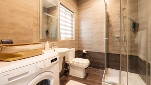 Un baño moderno con lavadora, inodoro y cabina de ducha con mampara de vidrio.