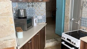 A compact kitchen with wooden cabinets, a microwave, a stove, and patterned backsplash tiles. - Serenity 2  studio apartment with small terrace (Ħal Qormi)