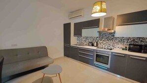 A modern kitchen with grey cabinets, a microwave, and a stove. There is a grey sofa and a small round table with a lamp. - Seaview apartment Sliema (Tas-Sliema)