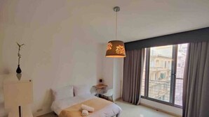 A hotel room with a bed, a desk, a chair, a lamp, and a window with curtains. - Seaview apartment Sliema (Tas-Sliema)
