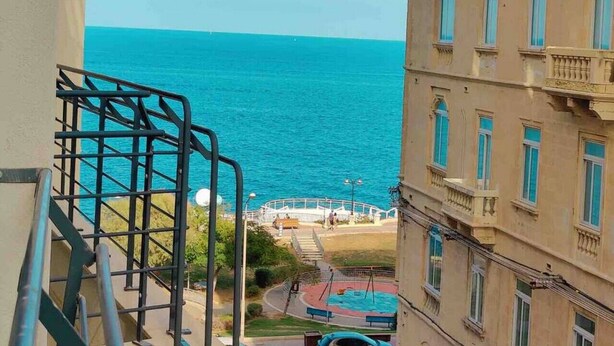 A view of a coastal area with a clear blue sea, a staircase leading down to a pedestrian path, and a building with balconies. - Seaview apartment Sliema (Tas-Sliema)