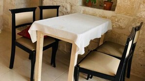 A stone-walled room with a table and two chairs, a small shelf with plants, and a television mounted on the wall. - Serenity 1 -cosy apartment in Qormi (Ħal Qormi)