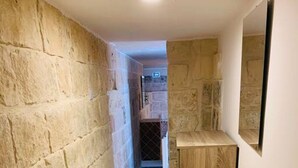 A hallway with stone walls, a wooden cabinet, and a tiled floor. - Serenity 1 -cosy apartment in Qormi (Ħal Qormi)
