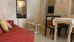 A living room with a red sofa, a small white table, and a dining table with chairs. - Serenity 1 -cosy apartment in Qormi (Ħal Qormi)