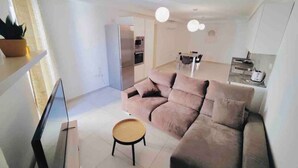 Ein modernes Wohnzimmer mit einer Couch, einem kleinen runden Tisch und einer Küche im Hintergrund.
