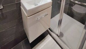 Ein modernes Badezimmer mit einem weißen Waschtisch, einer Duschkabine aus Glas und dunkel gefliesten Wänden.