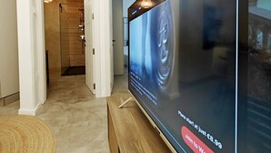 Een moderne woonkamer met een grote flatscreen televisie aan de muur, een houten salontafel en een gang naar een badkamer.