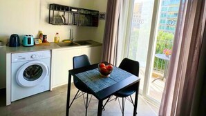 A compact living space with a washing machine, a dining table with chairs, and a view of a balcony with curtains. - The Valley Room 6 with parking on premises (San Ġiljan)