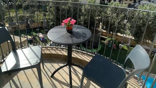 A balcony with a round table and chairs, a small potted plant, and a view of surrounding buildings. - The Valley Room 6 with parking on premises (San Ġiljan)