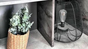 Een modern interieur met een marmeren wand, een zwarte vaas, een geweven mand met groene planten, en een zwarte metalen mand met een gloeilamp.