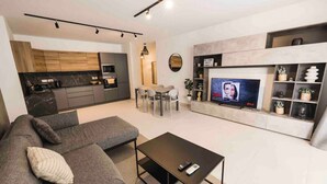 Een moderne woonkamer met een bank, salontafel, televisie en een keuken op de achtergrond.