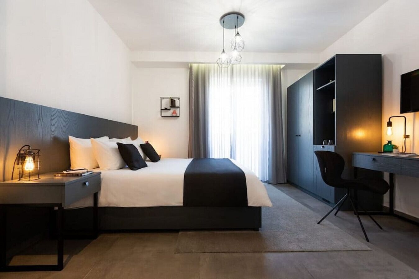A modern hotel room with a large bed, a desk, a chair, and a TV.