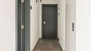 Ein schmaler Flur mit einer dunklen Tür am Ende, weißen Wänden und einem Lichtschalter an der Wand.