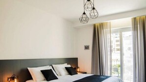 Ein Hotelzimmer mit einem Bett, zwei Nachttischen, einem Fenster mit Vorhängen und Blick nach draußen.