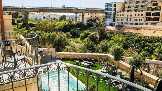 Ein Balkon mit Blick auf einen angelegten Garten, ein Schwimmbad und eine Brücke im Hintergrund.