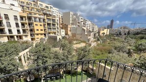 Ein Balkon mit zwei Stühlen und einem Tisch mit Blick auf eine Wohngegend mit mehrstöckigen Gebäuden und blauem Himmel.