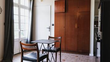 Quarto com guarda-roupa de madeira, uma mesa e duas cadeiras, e janela com cortinas.
