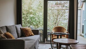 A living room with a grey sofa, a round wooden table, and a chair. - Bel Air, Accès Piscine - Jacuzzi Privé - Terrasse (Criel-sur-Mer)