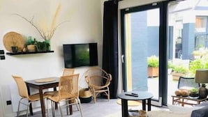 A modern living room with a sofa, a dining area with chairs, a TV, and a view of the outdoors. - Appartement - Piscine - Terrasse, Beau Séjour (Criel-sur-Mer)