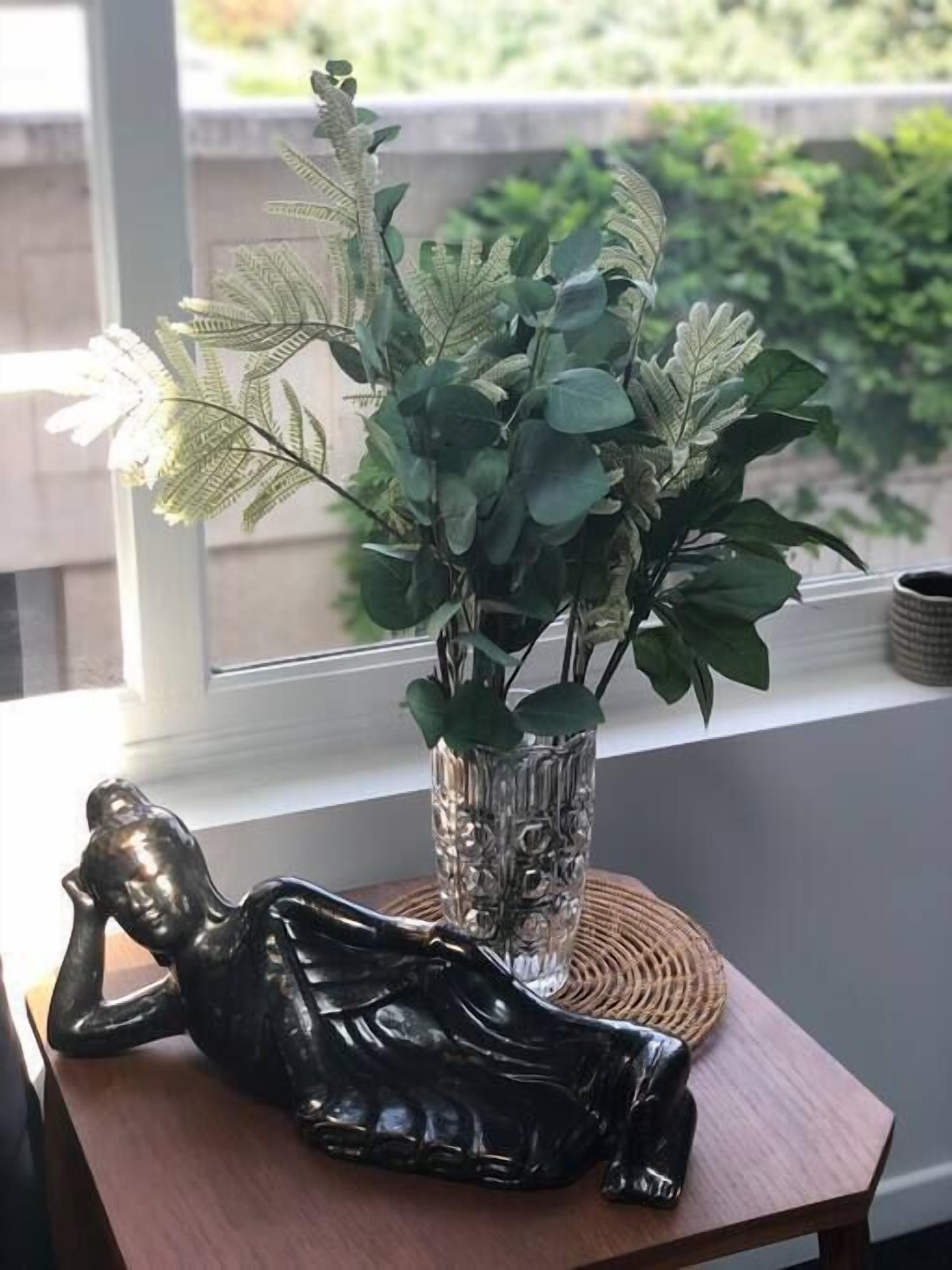 A room with a wooden table, a glass vase with green plants, and a black sculpture.