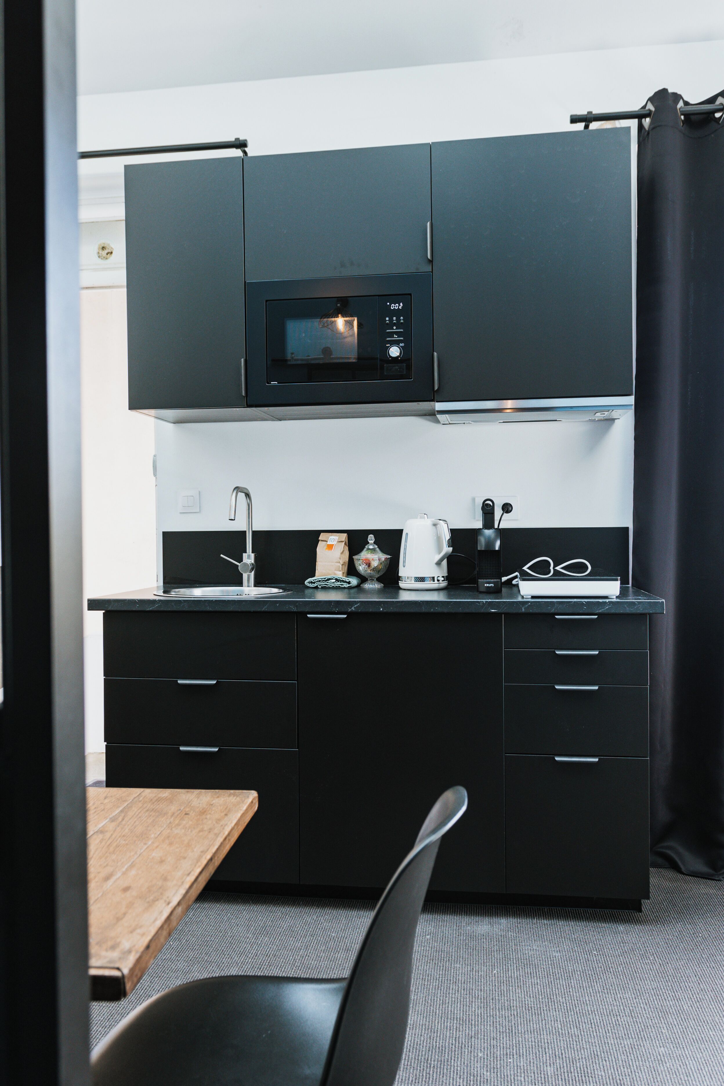 Een kleine keuken met zwarte kastjes, een magnetron, een waterkoker en een koffiezetapparaat.