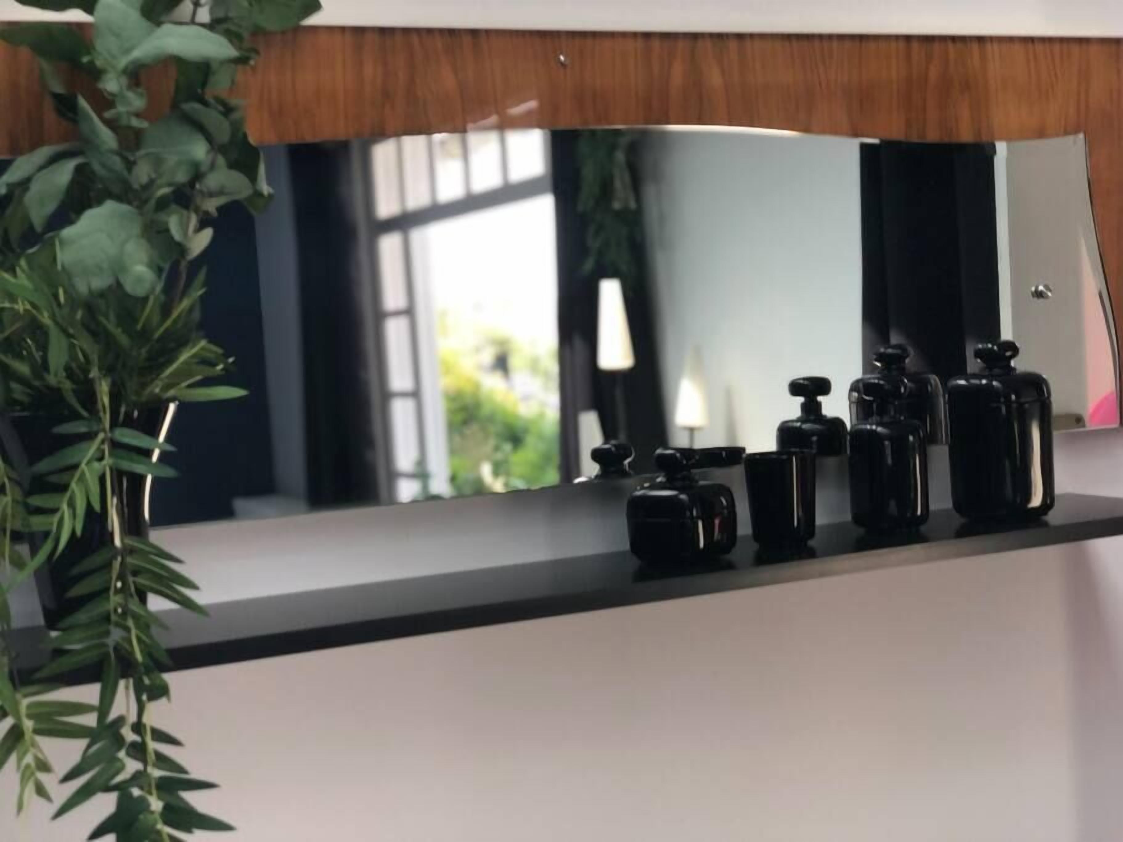 Un bagno con uno specchio, una pianta e articoli da toilette neri sul piano di appoggio.