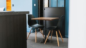 Un espace de bureau moderne avec une table en bois et deux chaises noires, un comptoir d’accueil sombre et un mur bleu avec une fenêtre.