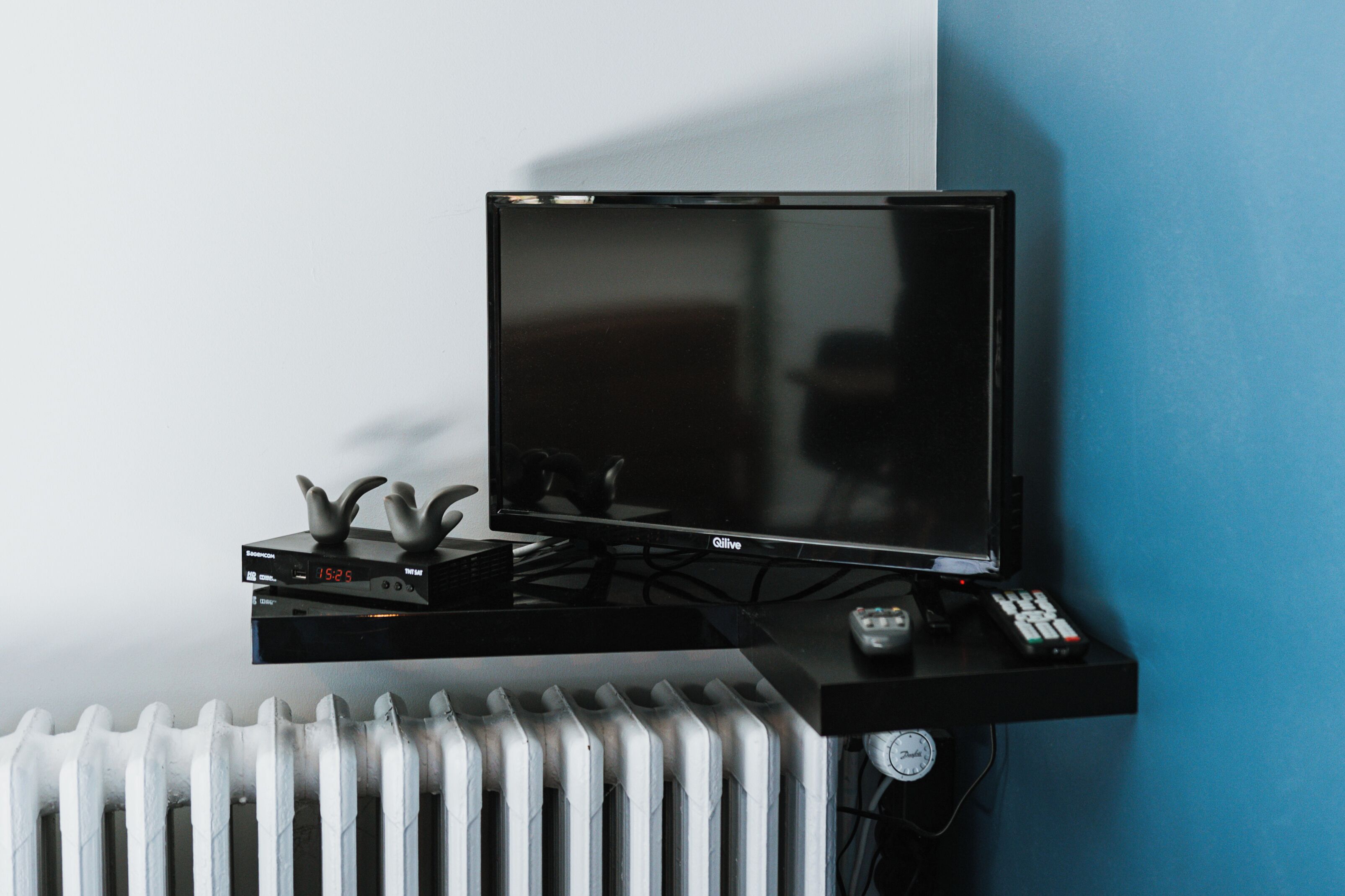 Un téléviseur noir posé sur un meuble noir, avec une télécommande et une horloge.