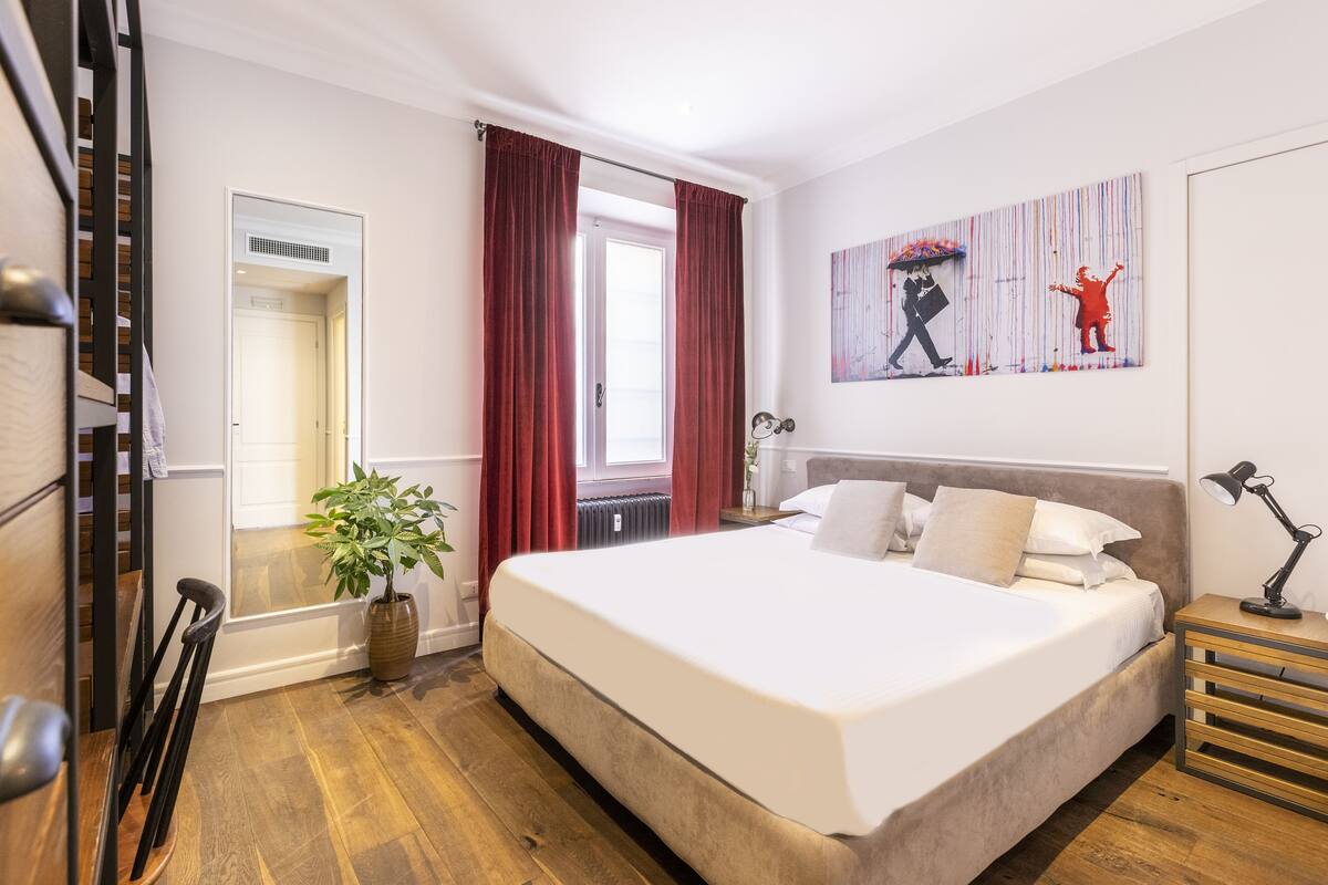 A modern bedroom with a large bed, a potted plant, a radiator, and a painting on the wall.