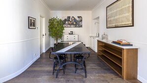 Un comedor moderno con una larga mesa, sillas, una planta en maceta y un cuadro de un paisaje urbano en la pared.