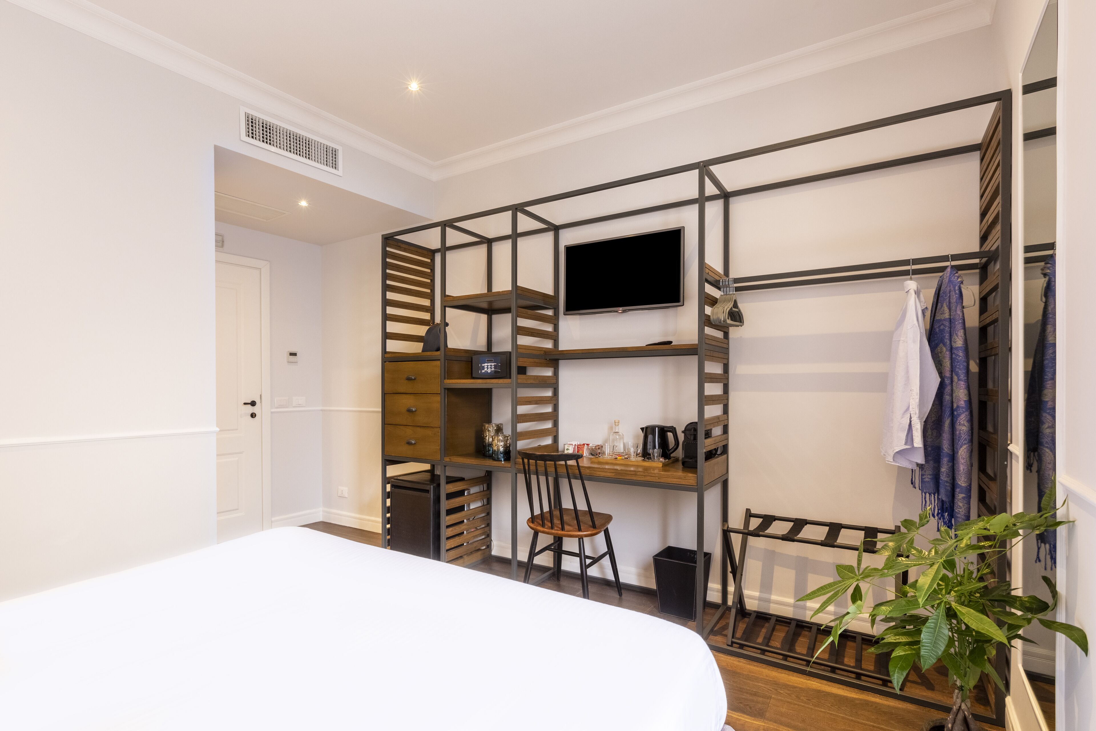 A compact room with a bed, a desk with a chair, a TV, and a shelving unit with storage.
