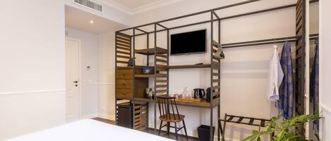 A compact room with a bed, a desk with a chair, a TV, and a shelving unit with storage.