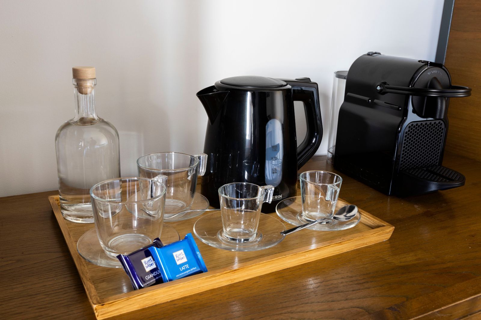 A coffee station with a coffee maker, a kettle, and several cups on a tray.