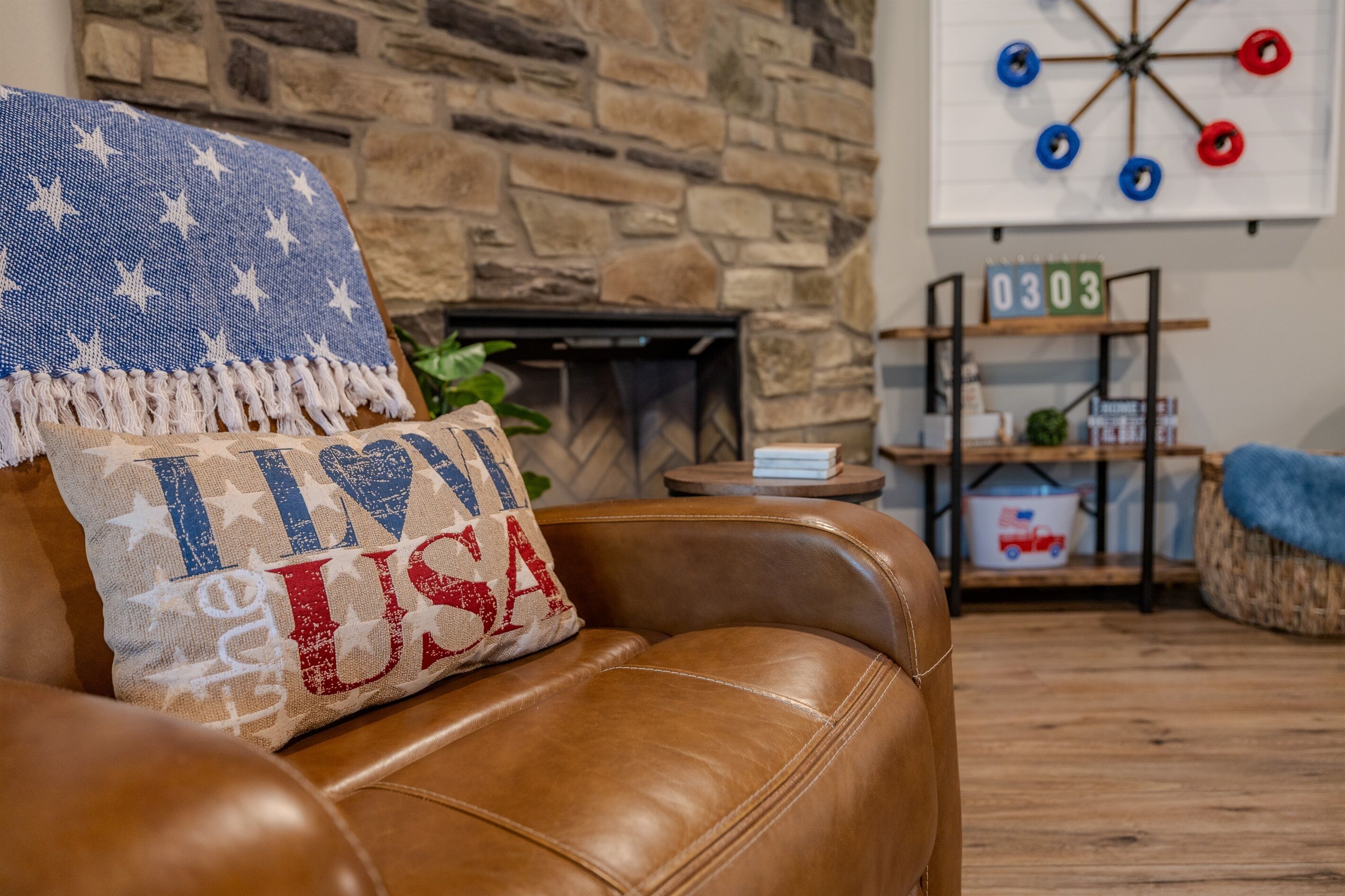 Ein Ledersofa mit einem Kissen im USA-Design, eine Steinwand, eine Dartscheibe und ein Regal mit Büchern und einer Pflanze.