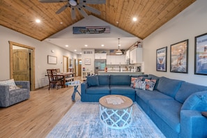 A spacious living area with a blue sofa, wooden ceiling, and a dining table with chairs.