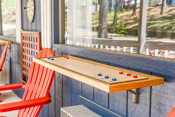 Une table de baby-foot avec un cadre en bois et des pions de jeu rouges et bleus, placée devant un mur bleu avec une fenêtre donnant sur une zone boisée.