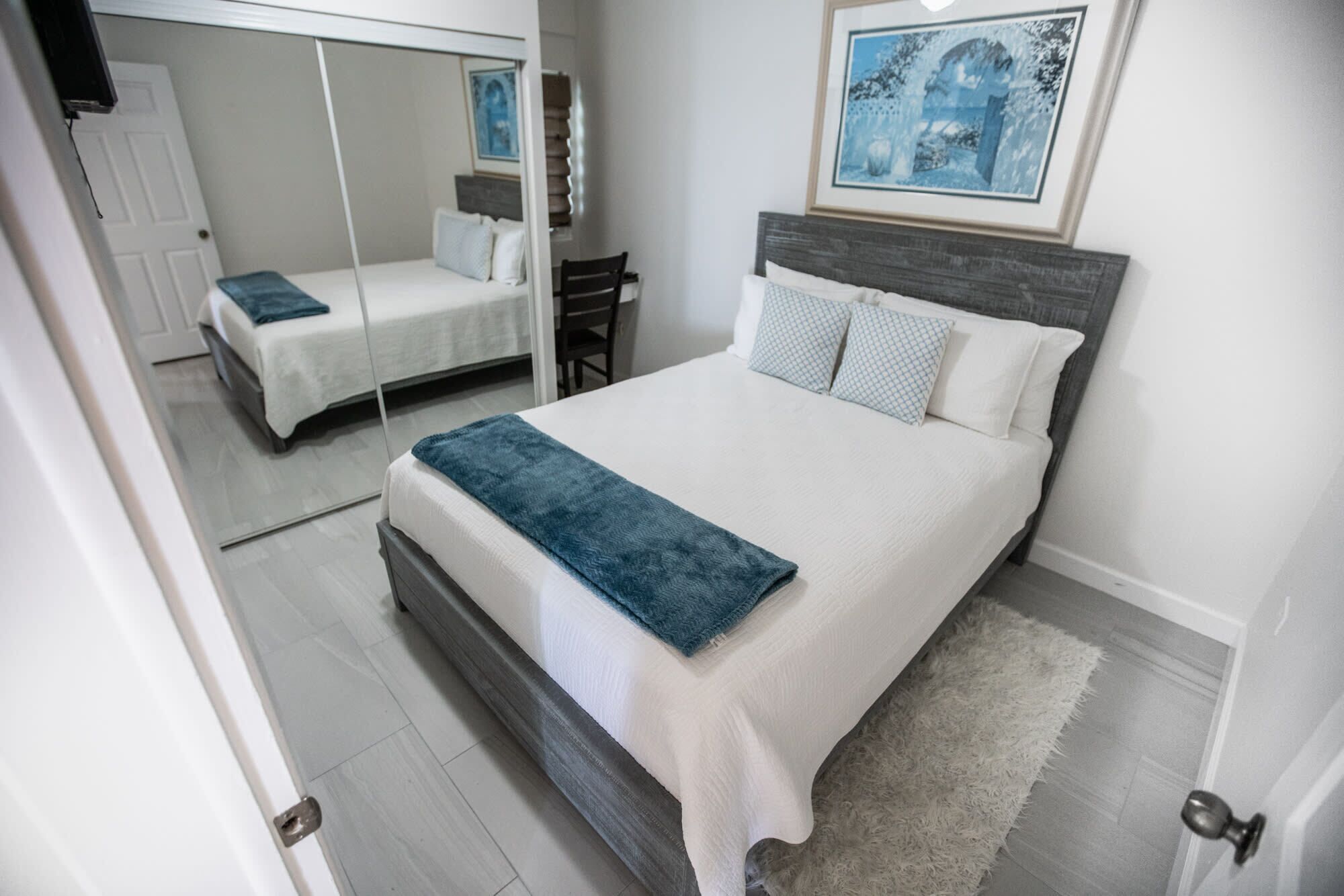Un dormitorio con una cama, una silla, un espejo y un cuadro en la pared.