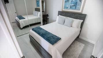 Una camera da letto con un letto, una sedia, uno specchio e un quadro appeso al muro.