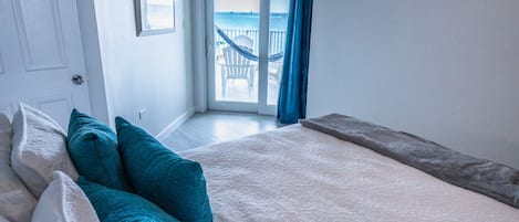 A bedroom with a bed, pillows, a view of the balcony, and a door.