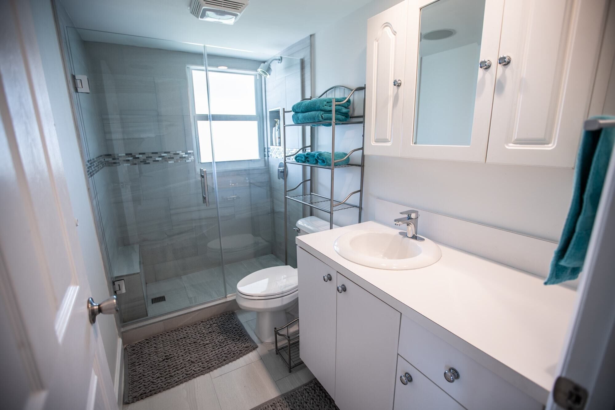 Un baño moderno con cabina de ducha de vidrio, un lavabo blanco y un estante empotrado con toallas.